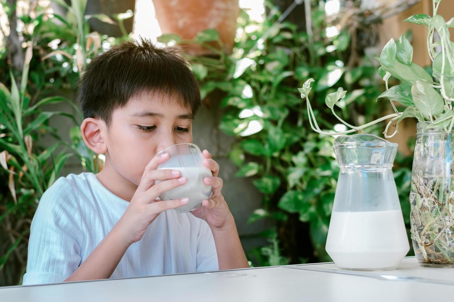 il ragazzo asiatico con una maglietta bianca sta bevendo un bicchiere di latte foto