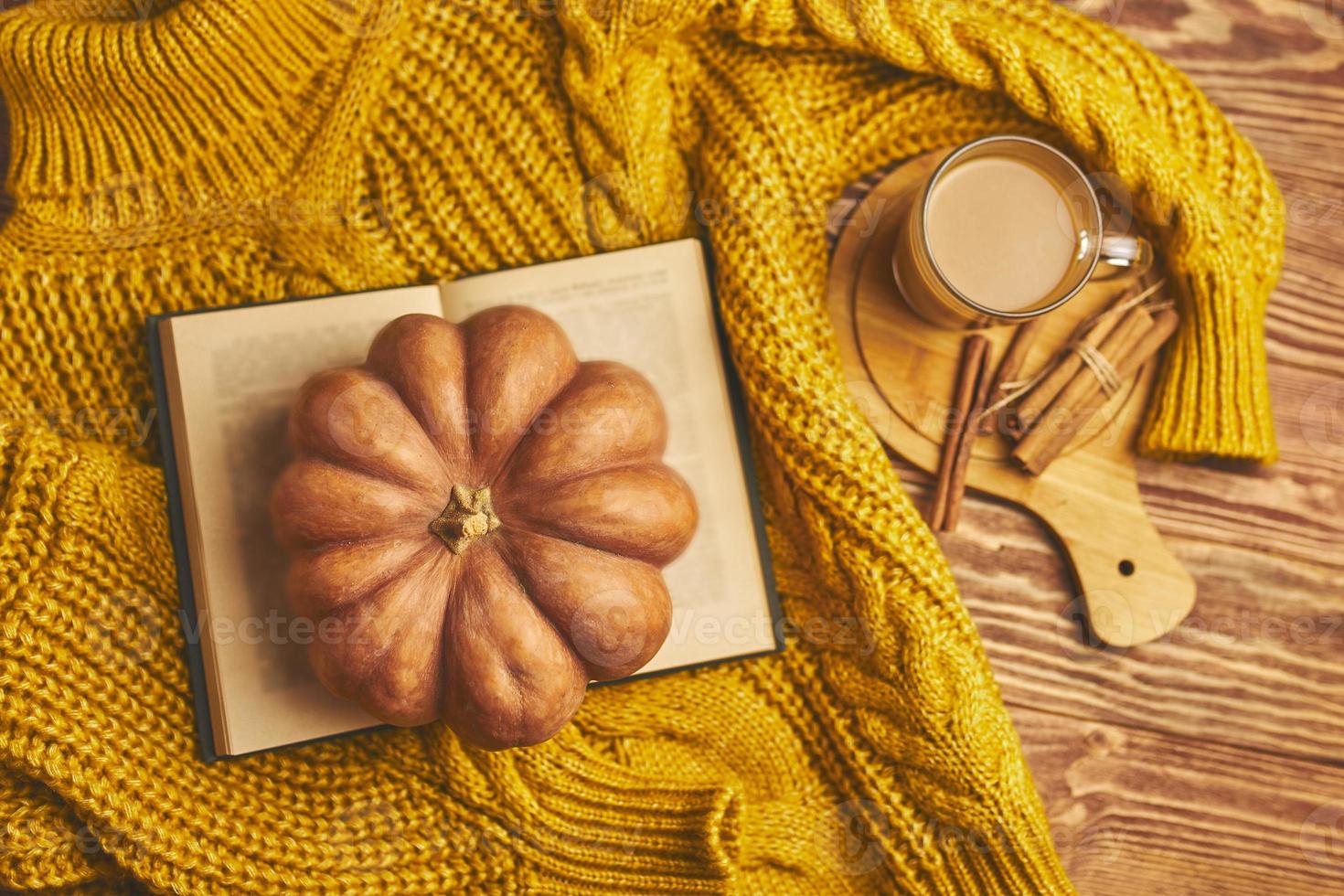 maglione caldo e accogliente, libro aperto e zucca su fondo di legno. foto