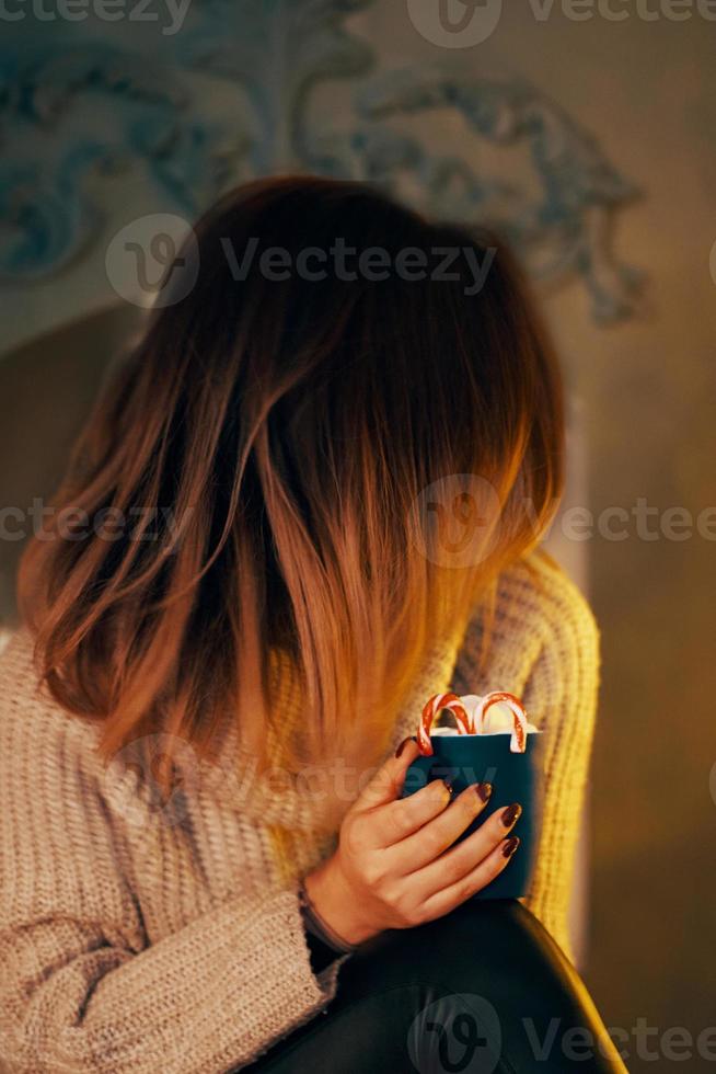 donna in maglione con una tazza di cacao davanti al caminetto. foto