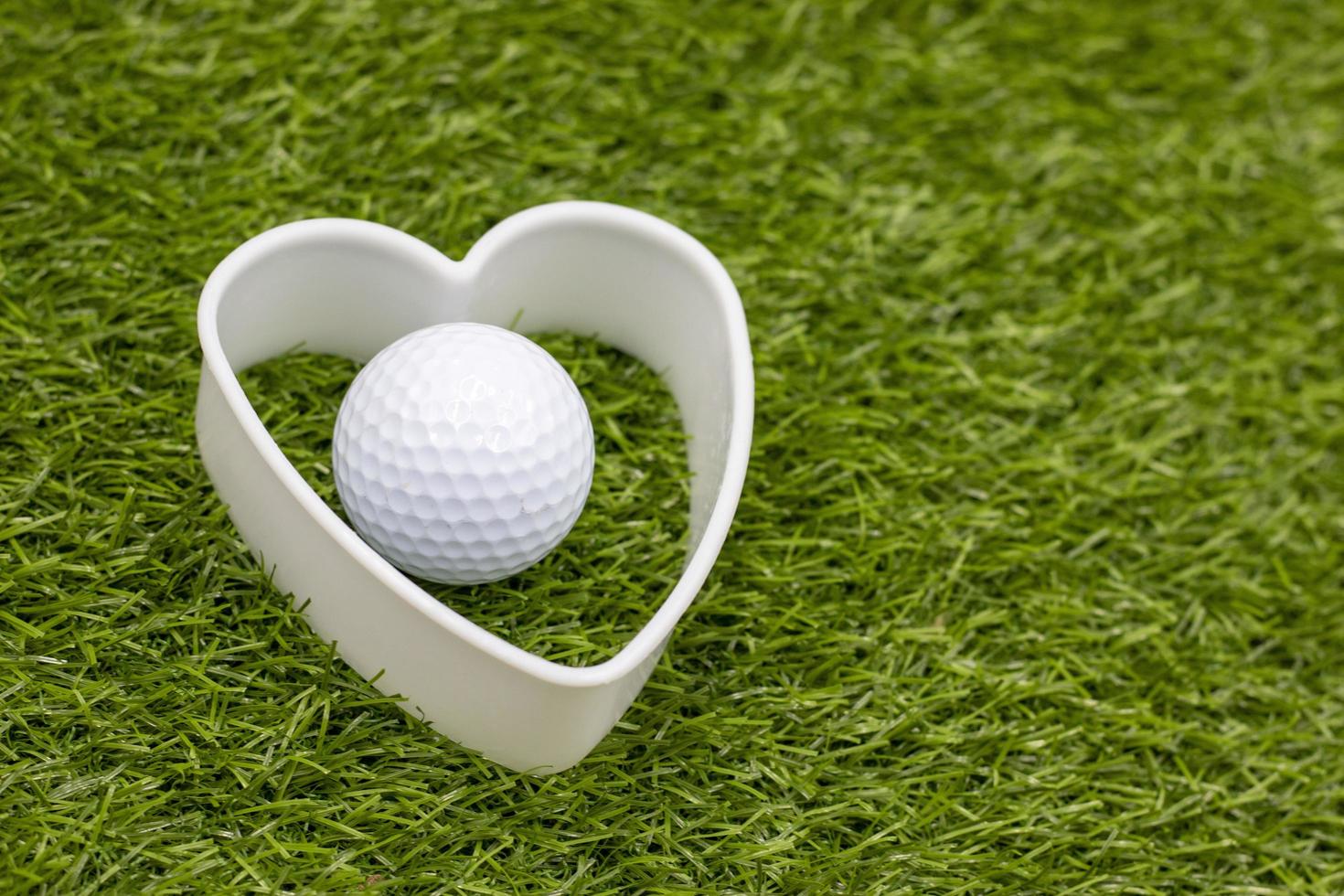 la pallina da golf con cuore bianco è sull'erba verde green foto