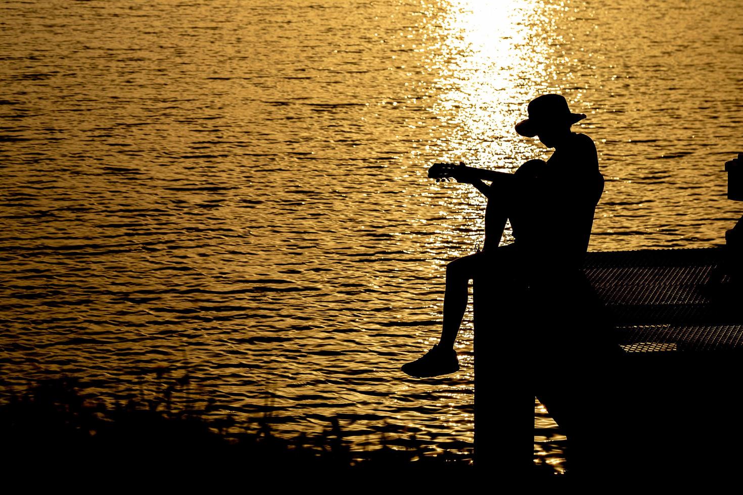 sagoma del chitarrista che suona una chitarra sul fiume sotto il tramonto foto