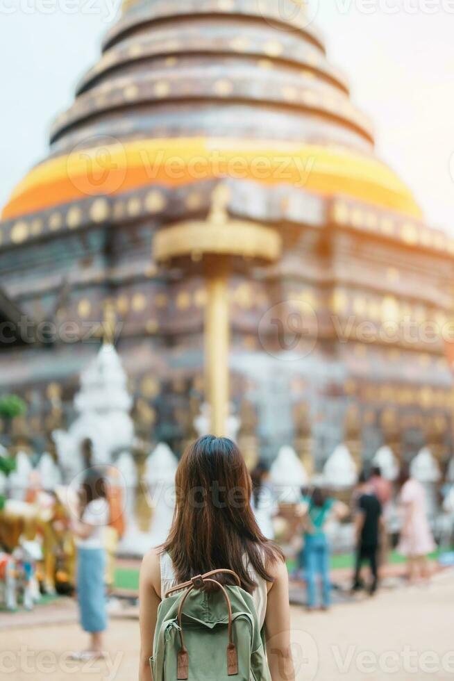 giovane asiatico donna viaggiatore nel bianca vestito con cappello e Borsa in viaggio nel wat Phra quello lampang luang, turista visitare a lampang, Tailandia.. Asia viaggiare, vacanza e estate vacanza concetto foto