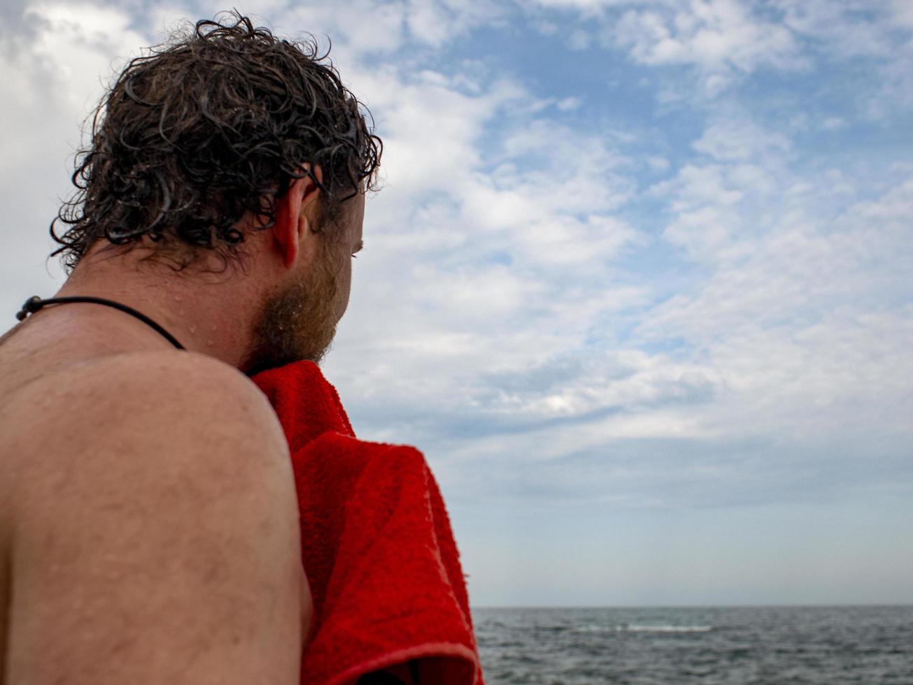 un uomo con la barba si asciuga un asciugamano dopo aver nuotato in mare.vista posteriore foto