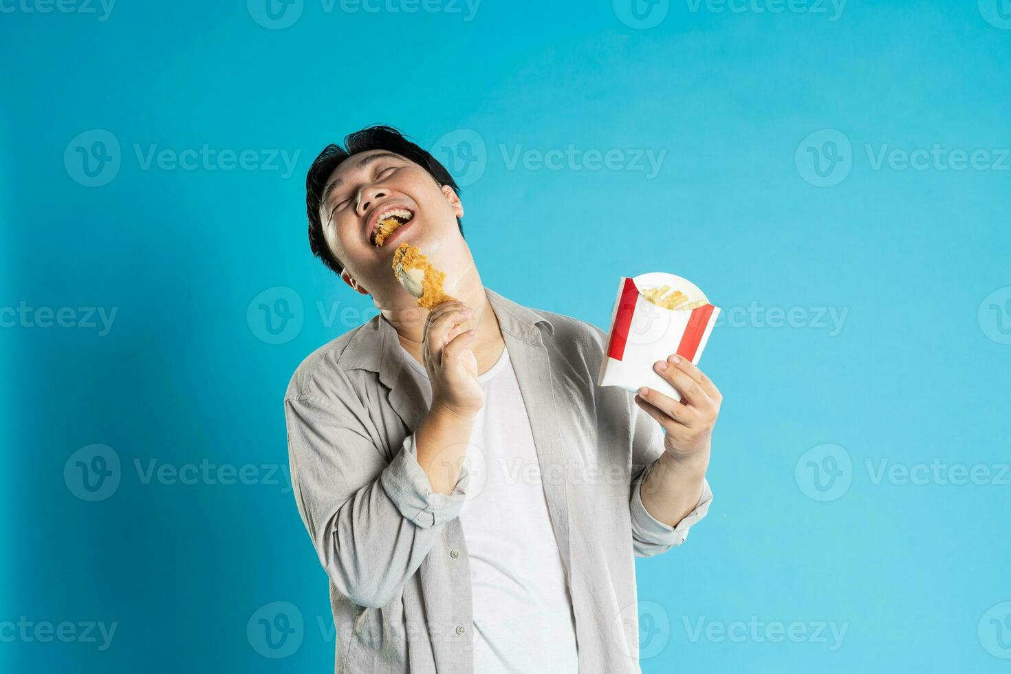 ritratto di asiatico uomo mangiare veloce cibo su blu sfondo foto