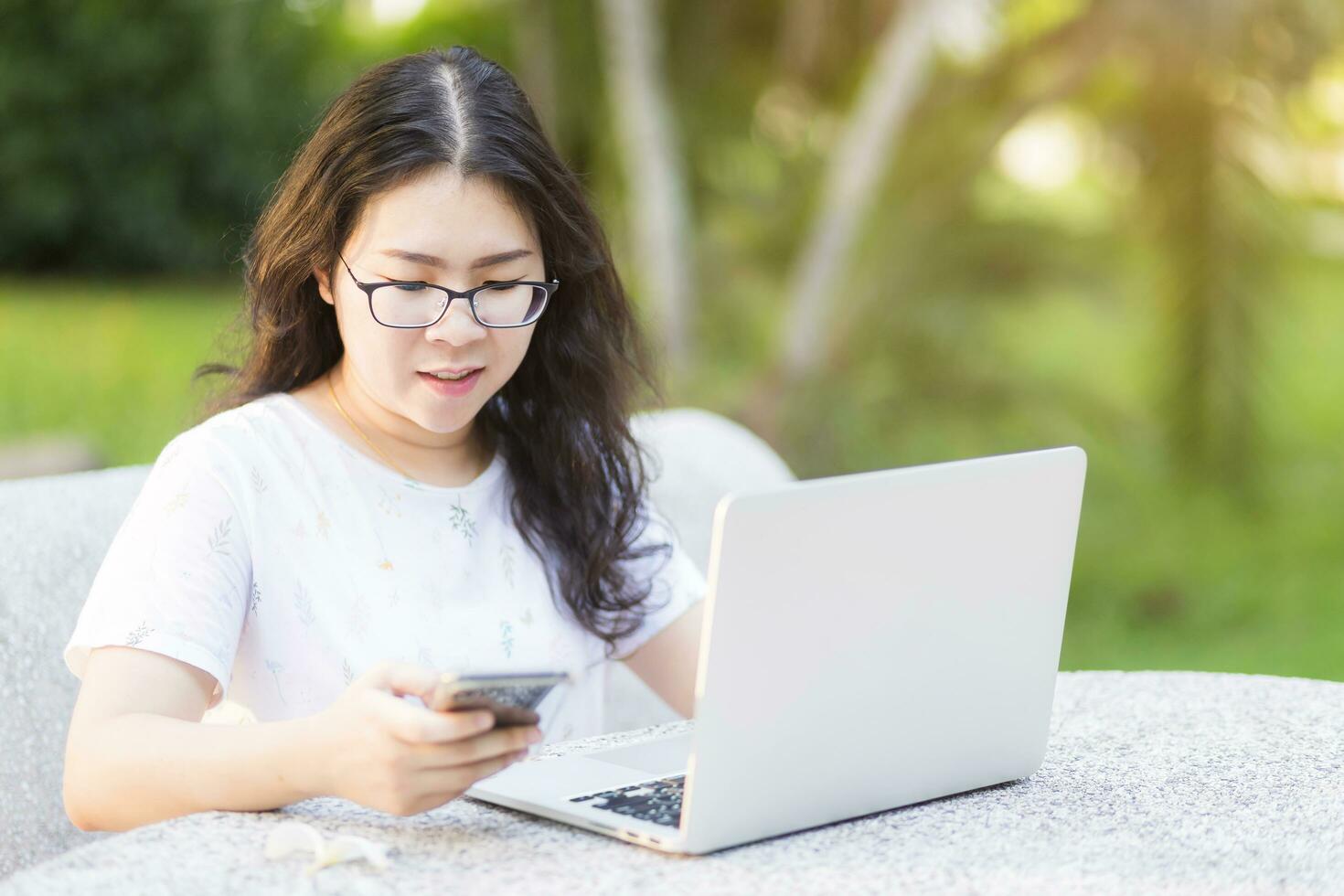 attività commerciale asiatico donna Lavorando con il computer portatile e smartphone nel a il parco su ufficio all'aperto. foto