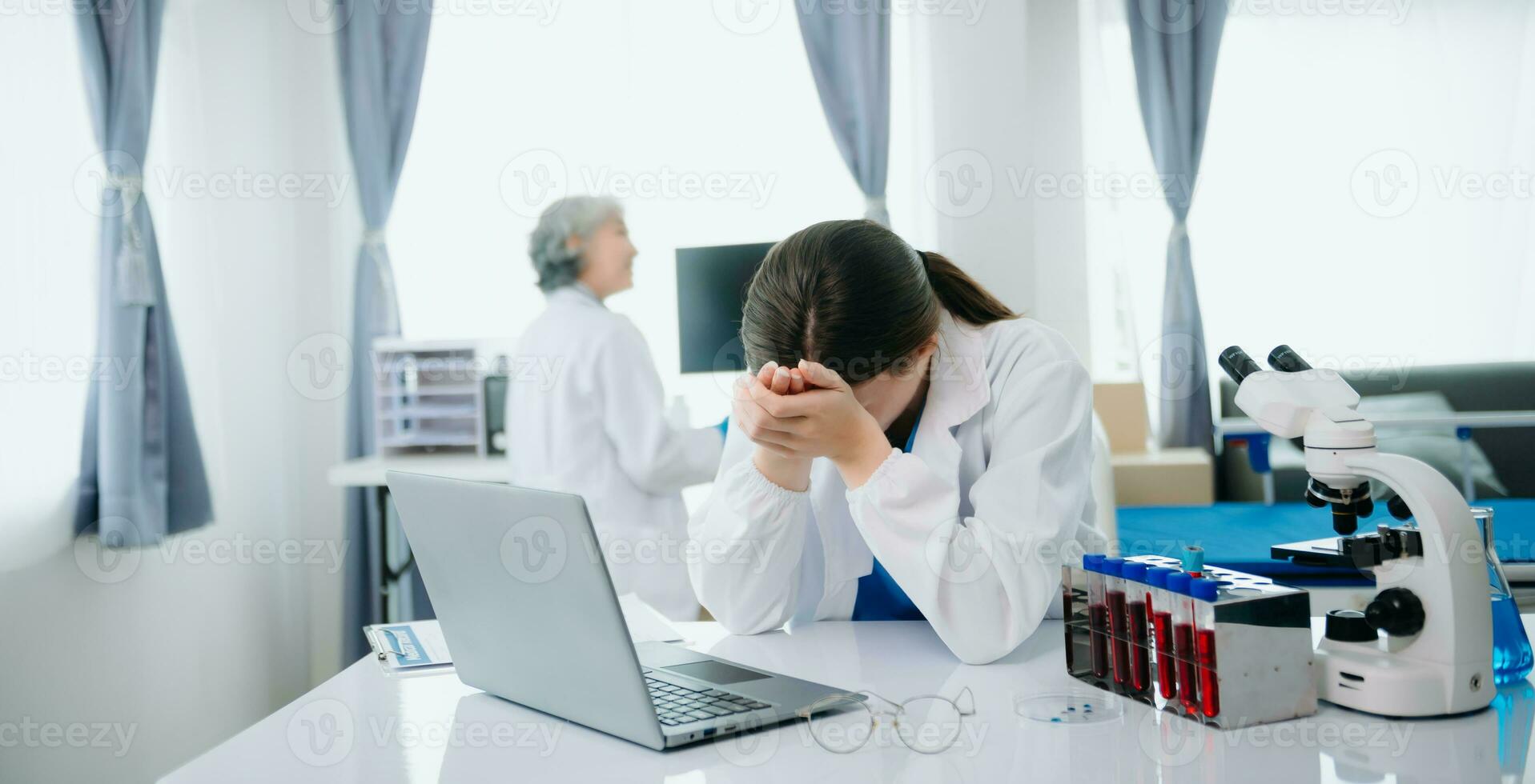 fiducioso giovane caucasico femmina medico nel bianca medico uniforme sedersi a scrivania Lavorando su computer. sorridente uso il computer portatile Scrivi nel medico rivista foto