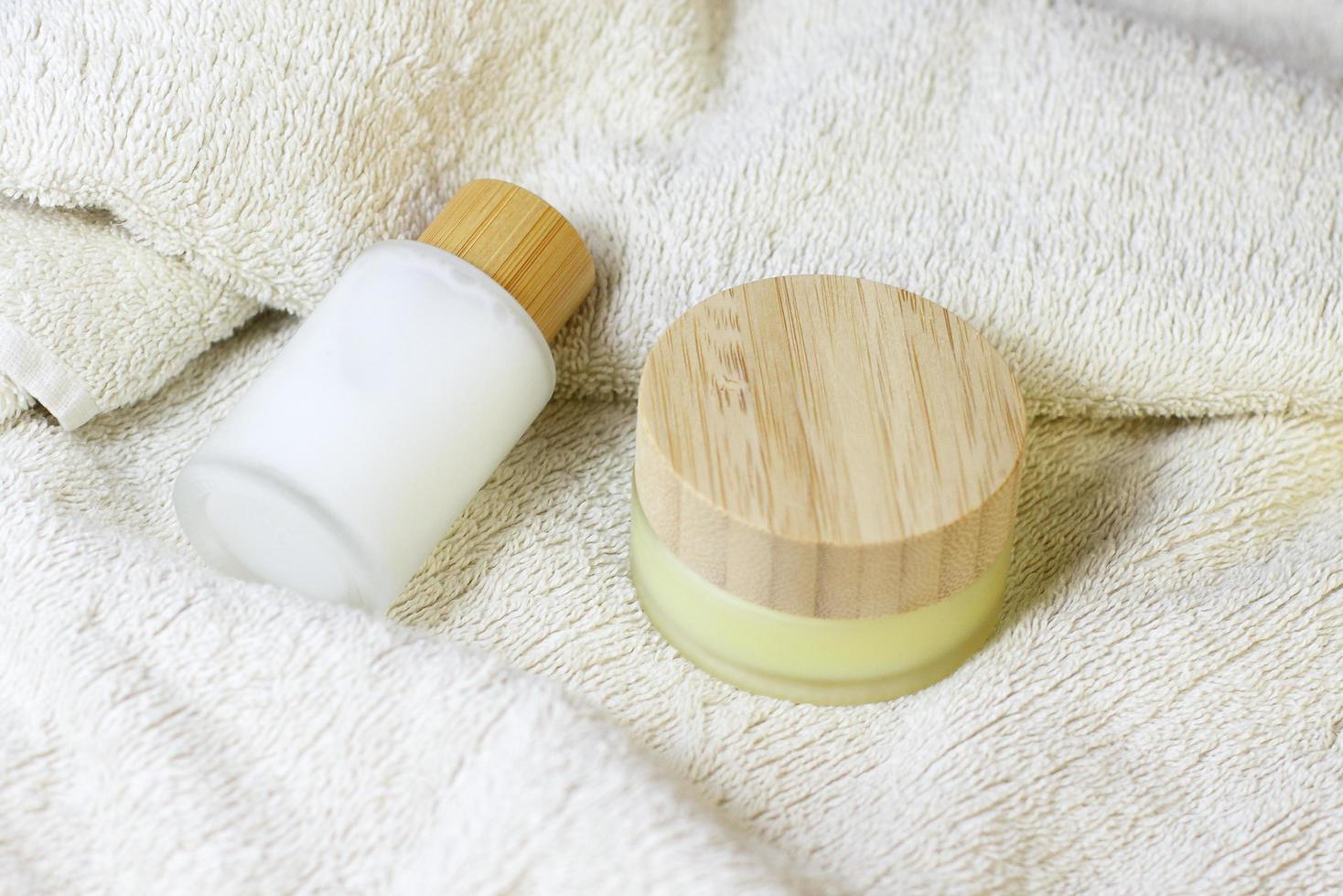 spazzola naturale in legno per il massaggio della pelle secca su asciugamano bianco con flaconi cosmetici in cristallo con piano in legno di bambù foto