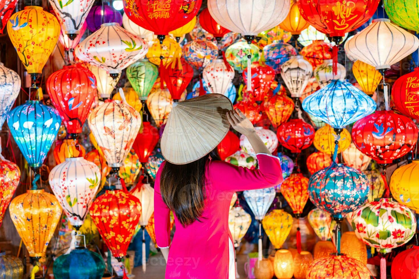 giovane femmina turista nel vietnamita tradizionale vestito guardare a carta ornamentale lanterne nel Hoi un antico cittadina foto