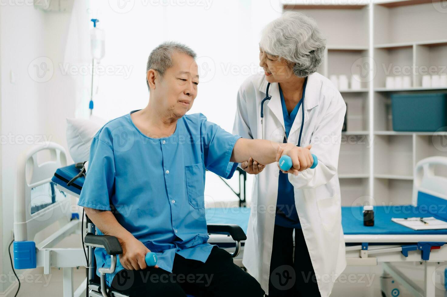 asiatico fisioterapista porzione anziano uomo paziente allungamento braccio durante esercizio corretta con manubrio nel mano durante formazione mano nel letto nel clinica foto
