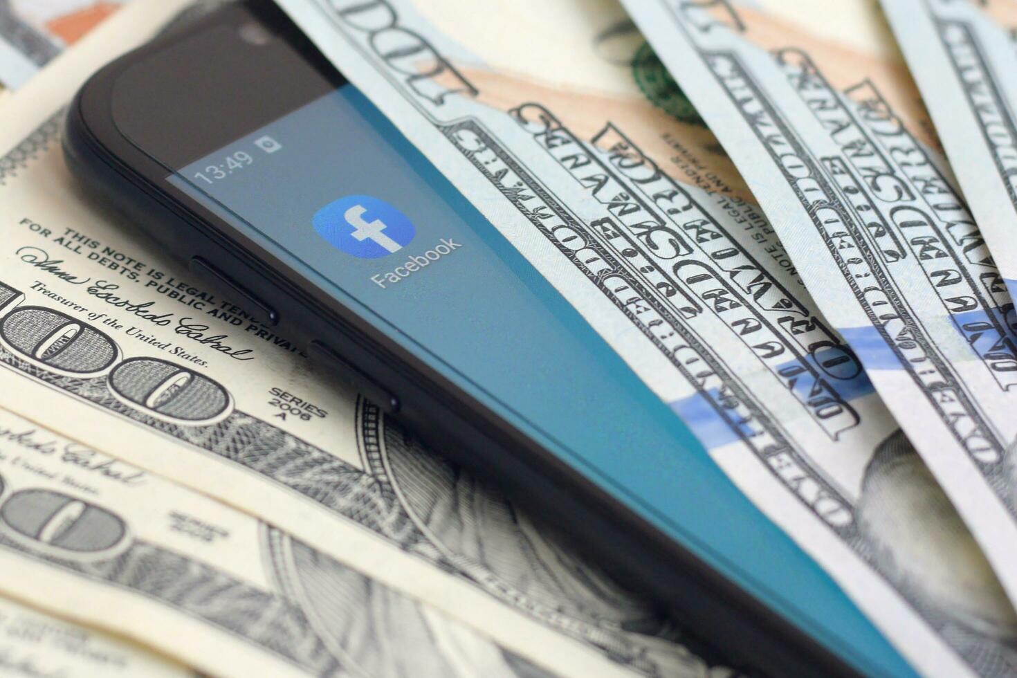 smartphone schermo con Facebook App e lotto di centinaio dollaro fatture. attività commerciale e sociale networking concetto foto