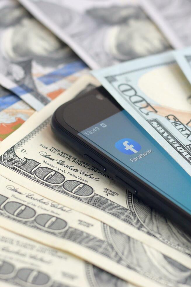 smartphone schermo con Facebook App e lotto di centinaio dollaro fatture. attività commerciale e sociale networking concetto foto