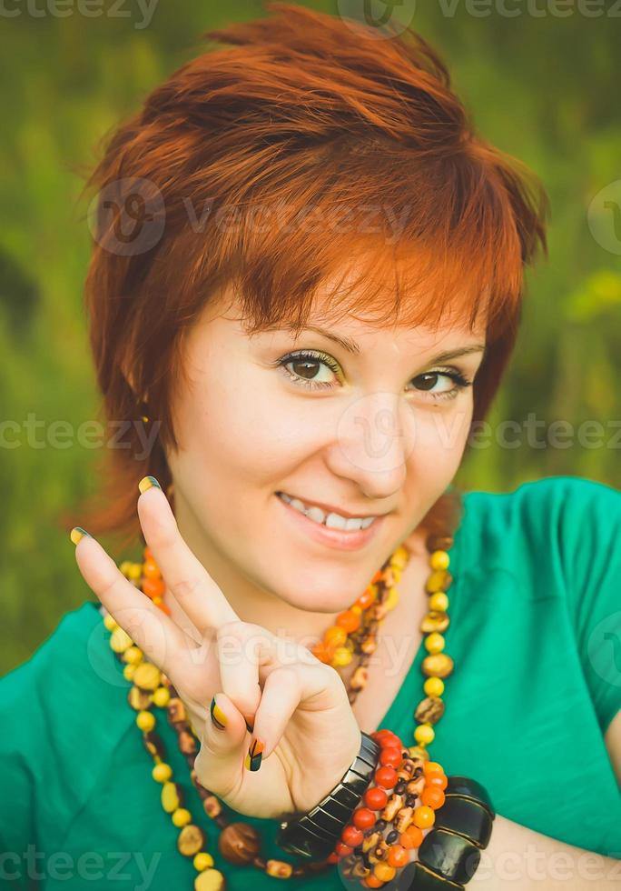 la giovane donna felice mostra la mano di vittoria. ragazza hippie dai capelli rossi in natura. giornata internazionale della pace foto