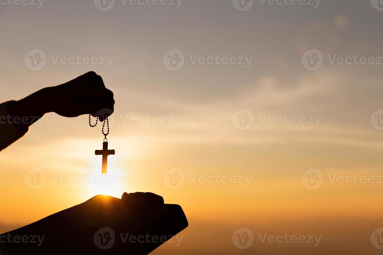 siluetta delle mani di giovane donna che tengono la Sacra Bibbia e sollevamento della croce cristiana con sfondo tramonto chiaro. foto