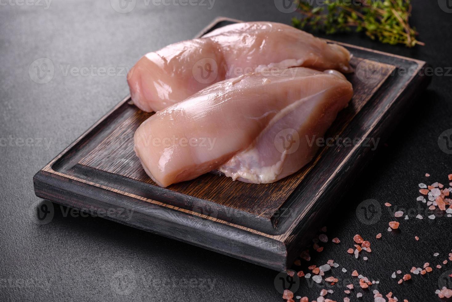 filetto di pollo fresco su un tavolo di cemento scuro con spezie ed erbe aromatiche foto