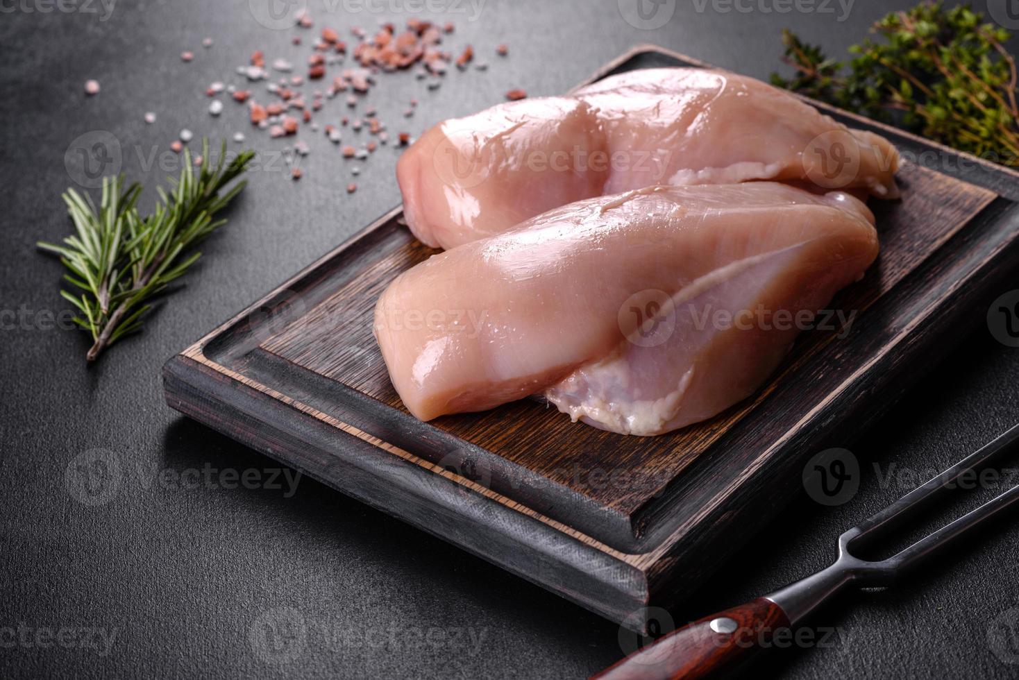 filetto di pollo fresco su un tavolo di cemento scuro con spezie ed erbe aromatiche foto