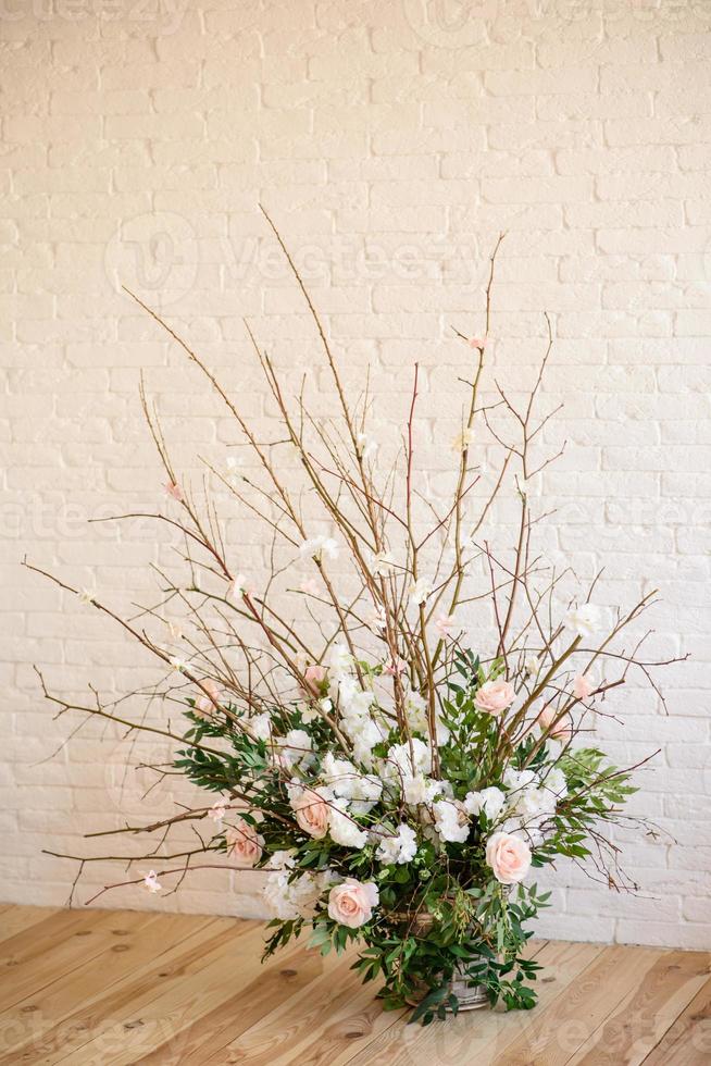 decorazioni di rami con bellissimi fiori rosa e bianchi nel cesto sullo sfondo di un muro di mattoni bianchi foto