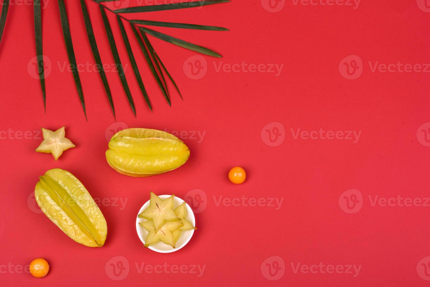 carambola di frutta, accessori da spiaggia e fogliame di una pianta tropicale su carta colorata foto