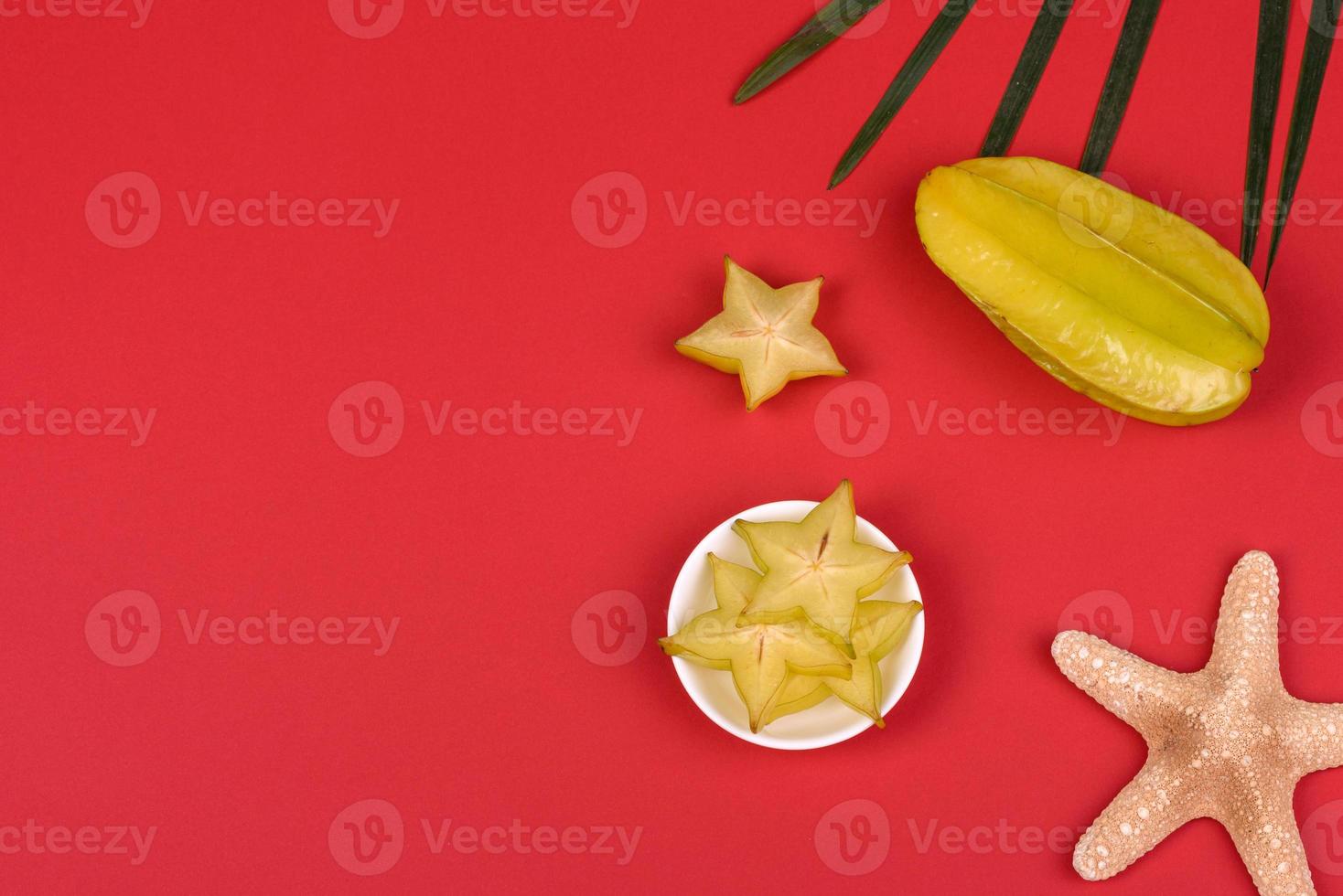 carambola di frutta, accessori da spiaggia e fogliame di una pianta tropicale su carta colorata foto