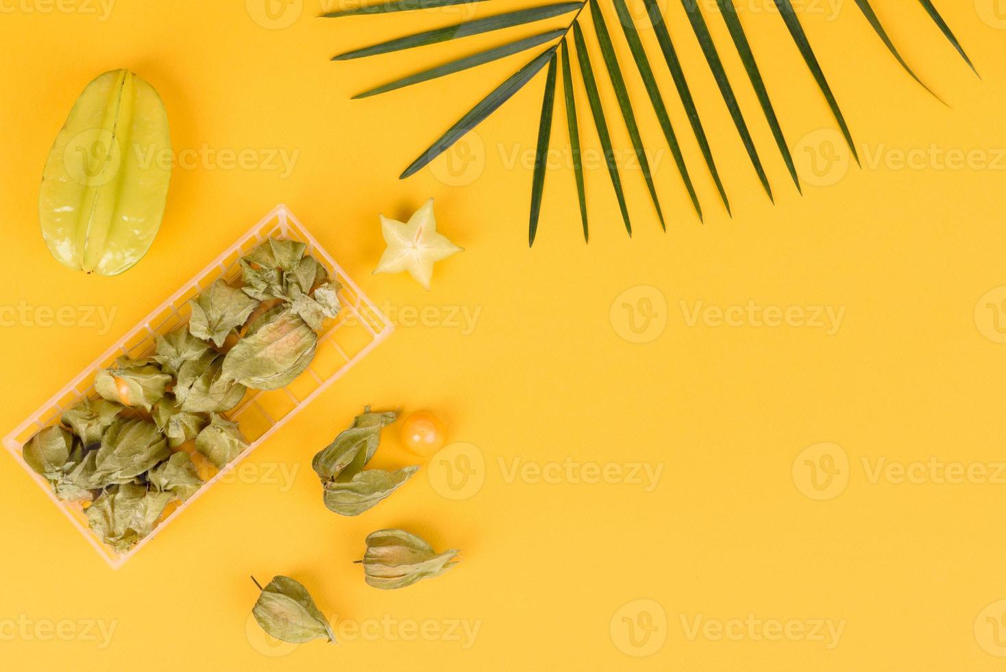 carambola di frutta, accessori da spiaggia e fogliame di una pianta tropicale su carta colorata foto