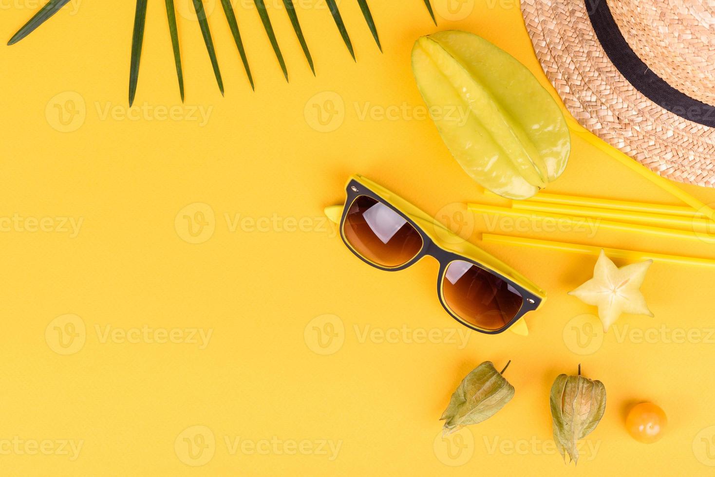 carambola di frutta, accessori da spiaggia e fogliame di una pianta tropicale su carta colorata foto