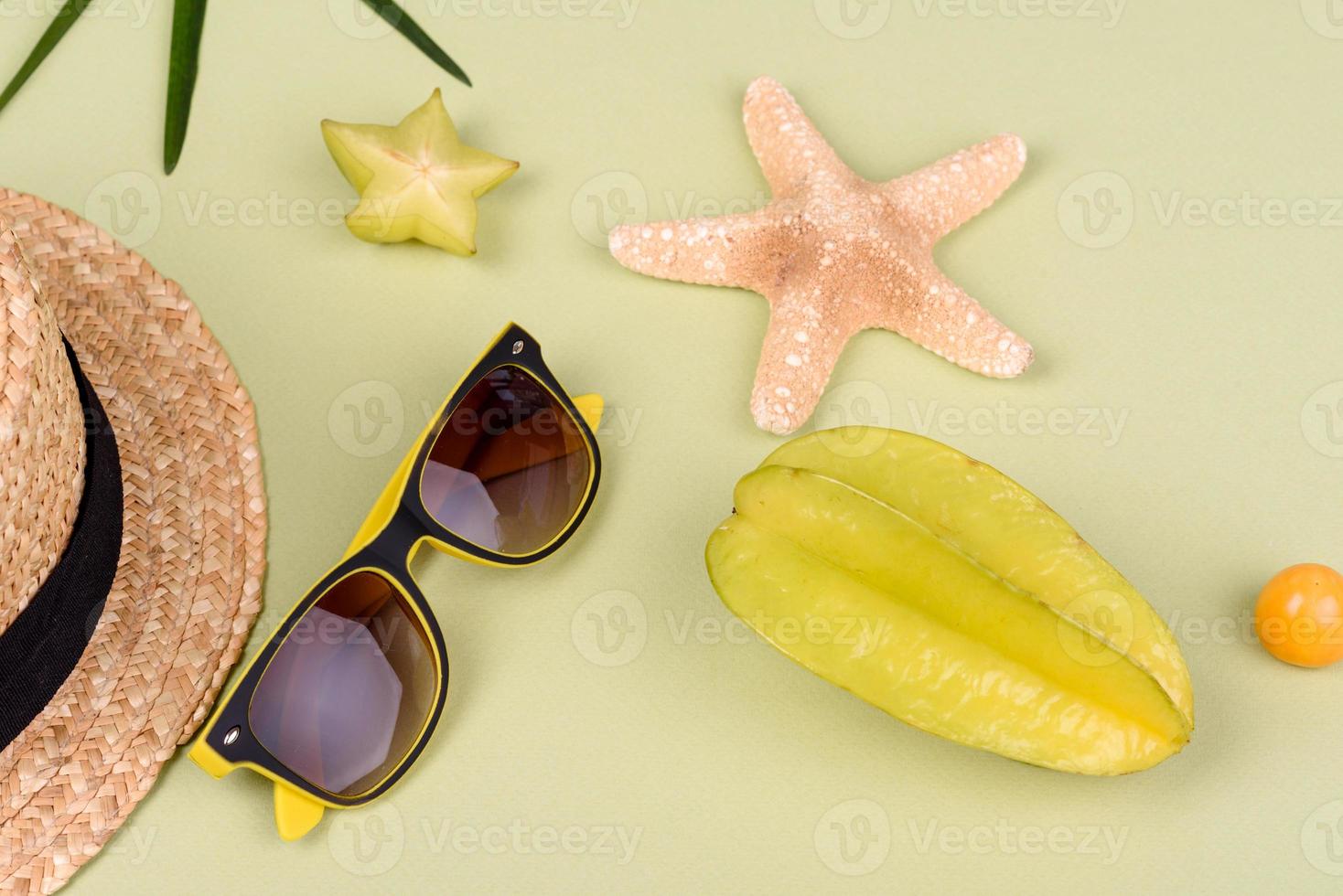 carambola di frutta, accessori da spiaggia e fogliame di una pianta tropicale su carta colorata foto