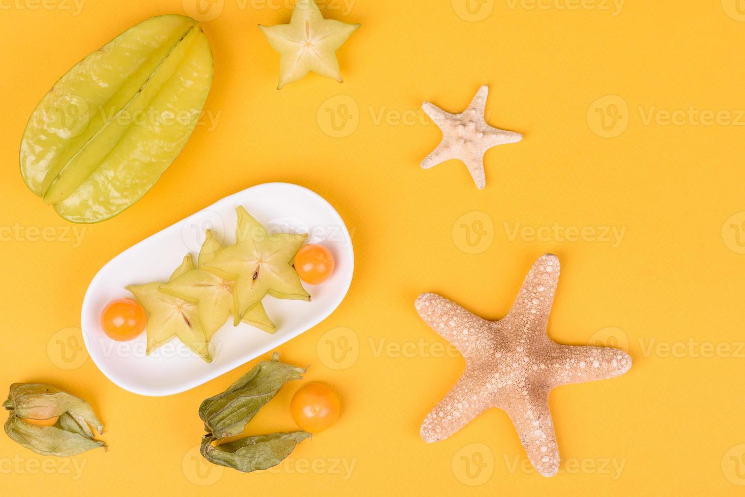 carambola di frutta, accessori da spiaggia e fogliame di una pianta tropicale su carta colorata foto