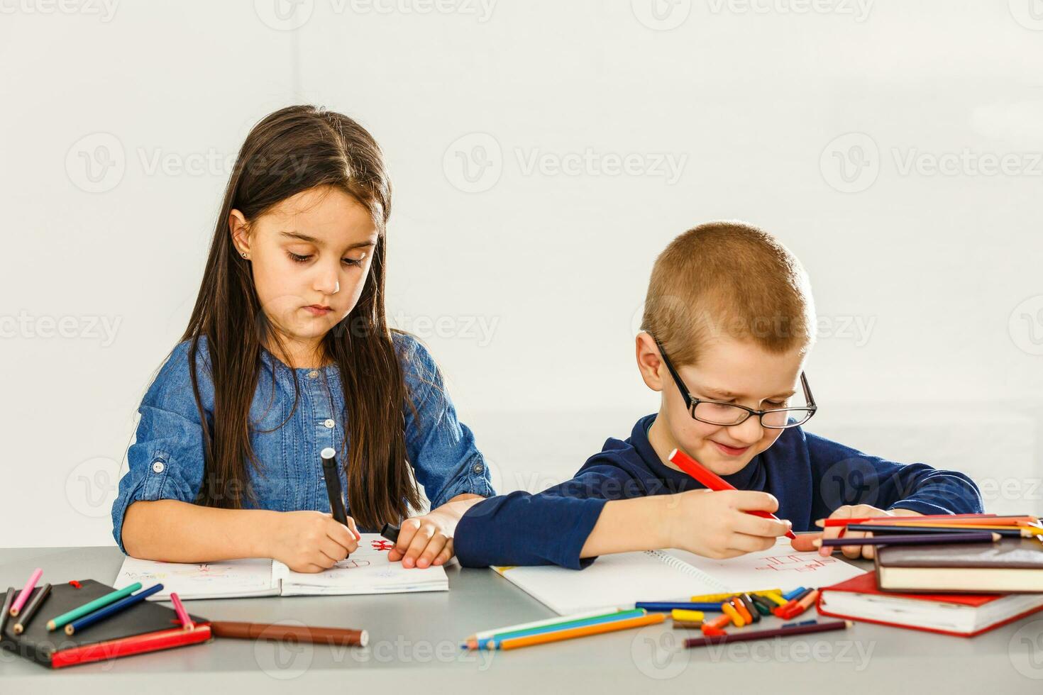Due sorridente poco bambini a il tavolo disegnare con pastelli, isolato su bianca foto