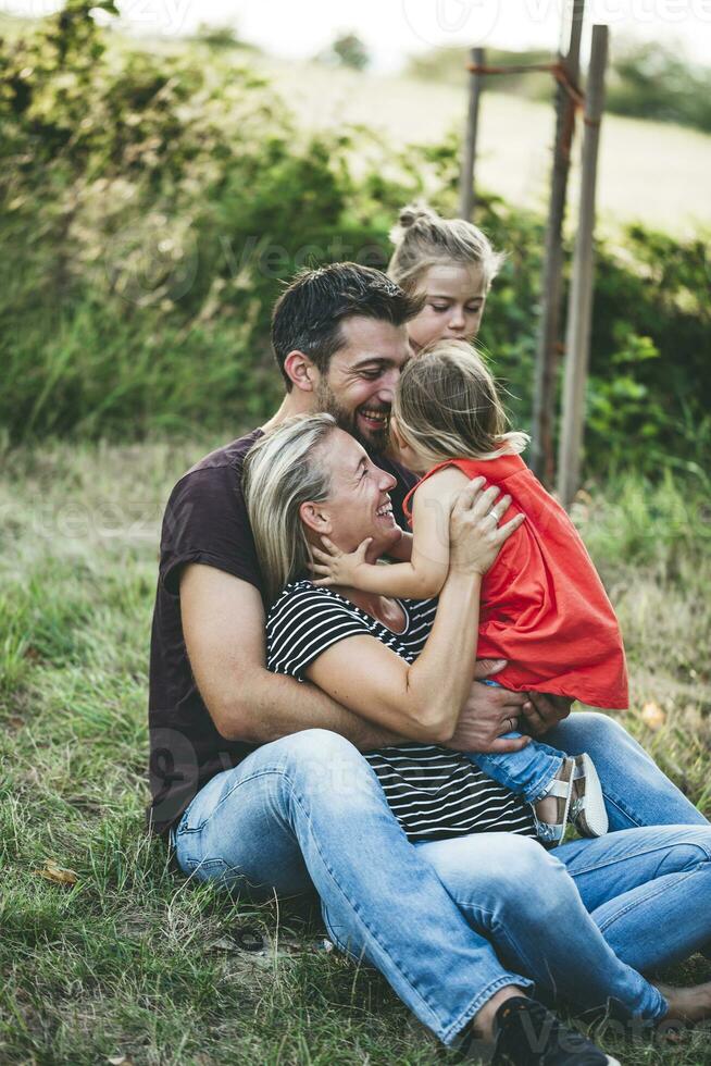 contento famiglia con Due figlie seduta su un' prato foto