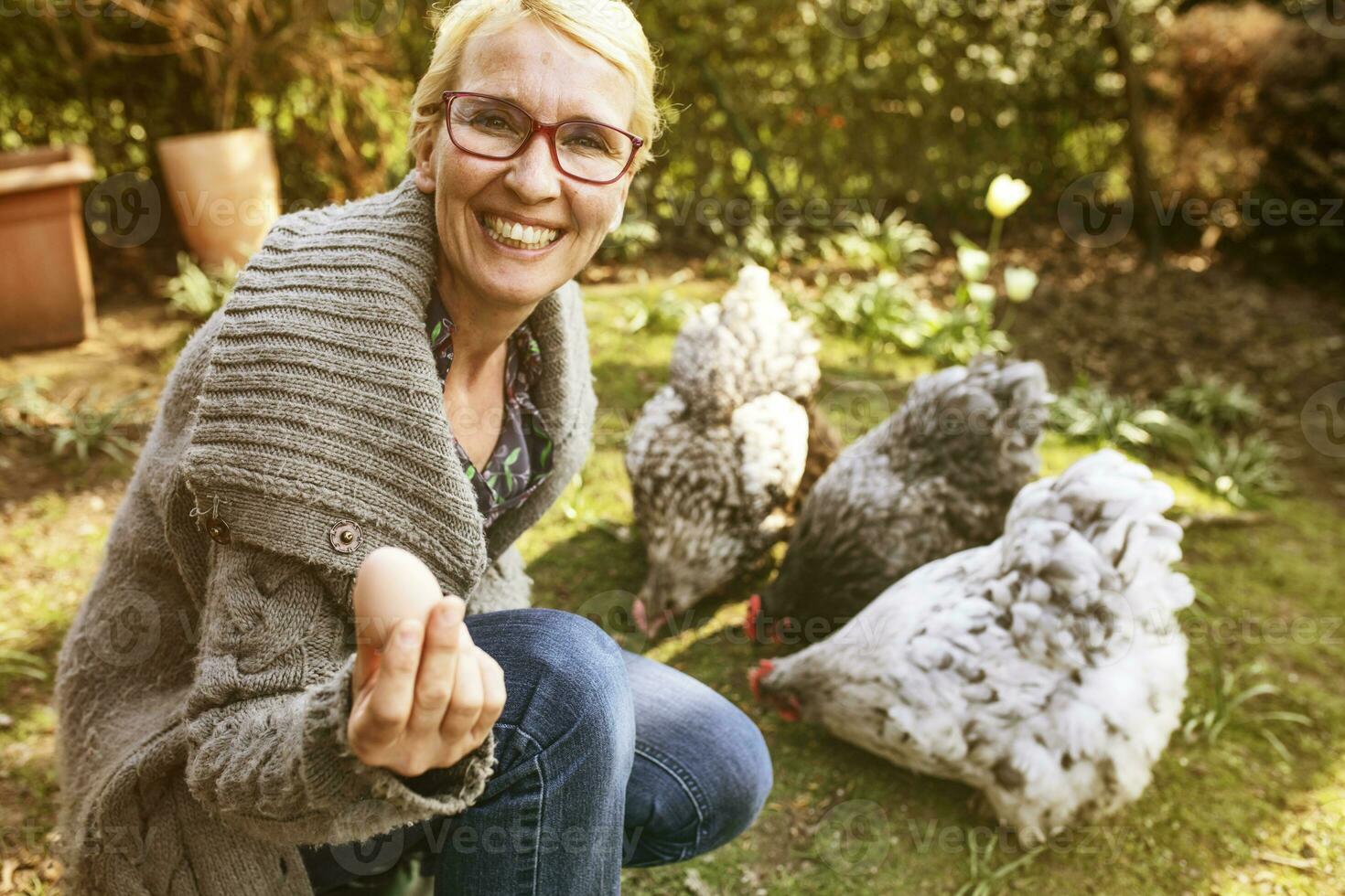 ritratto di contento donna nel giardino con sua orpington galline mostrando uovo foto