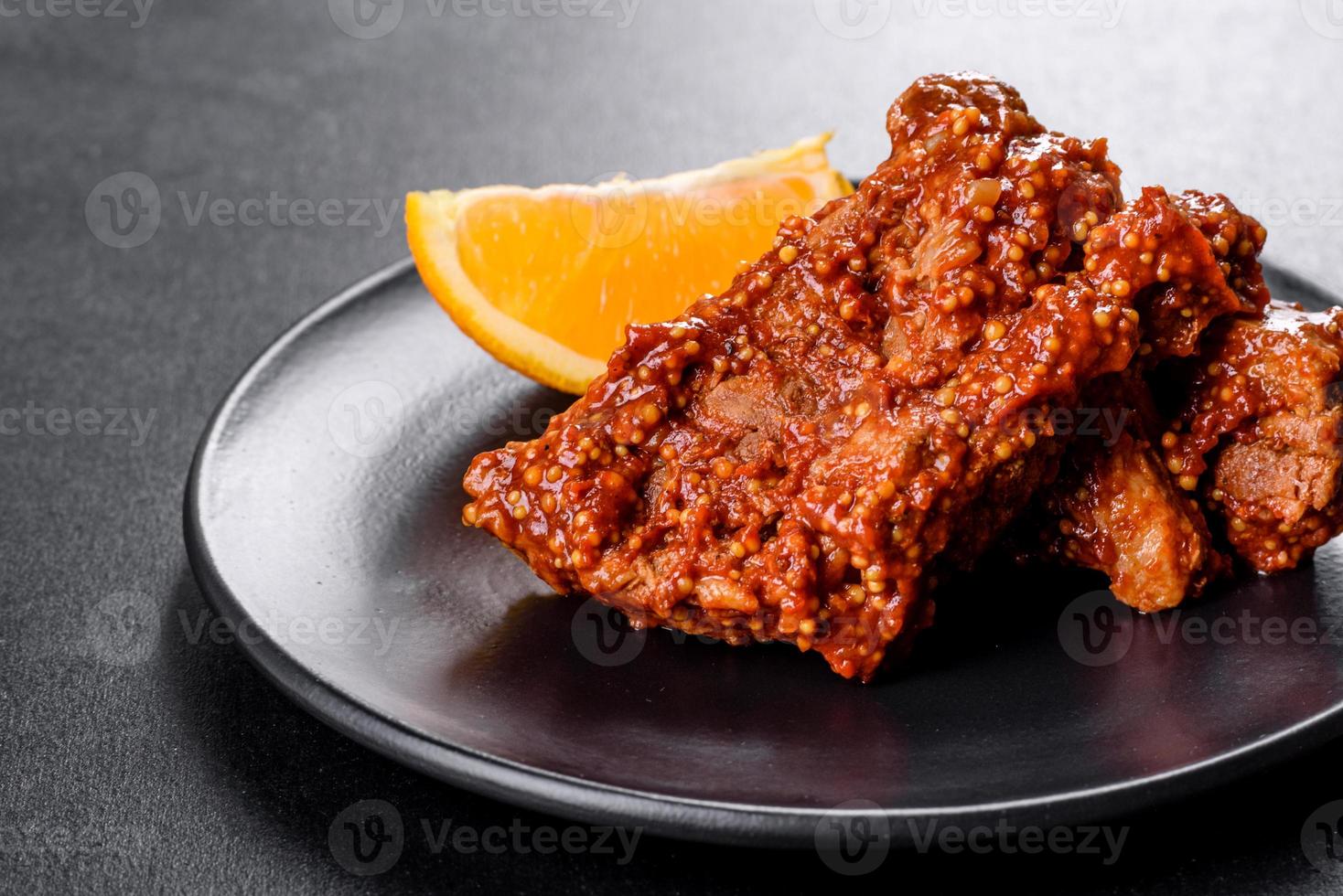 deliziose costolette di maiale al forno fresche con arancia su un piatto nero foto
