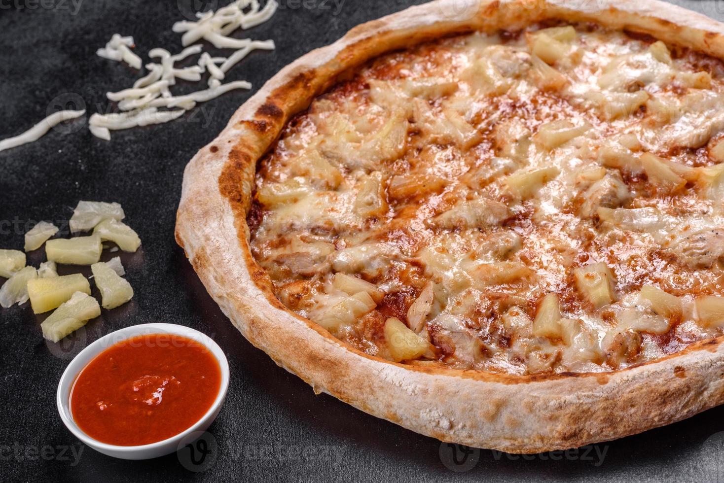 pizza italiana fresca e deliziosa con pollo, pomodori e ananas su uno sfondo di cemento scuro foto