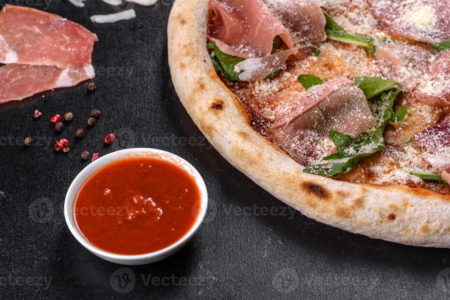 pizza italiana fresca e deliziosa con prosciutto su uno sfondo di cemento scuro foto