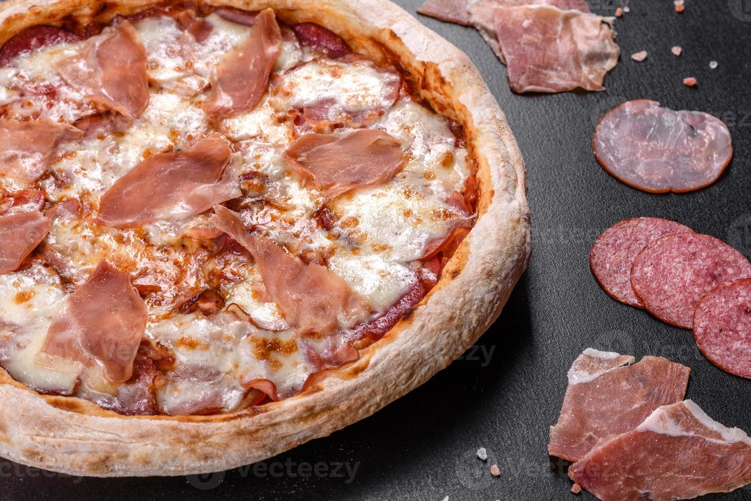 pizza italiana fresca e deliziosa con prosciutto su uno sfondo di cemento scuro foto