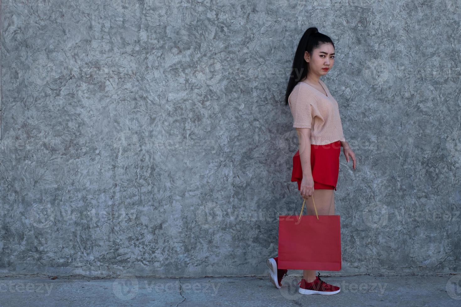 ritratto di una bellissima giovane donna asiatica che indossa una maschera facciale con in mano borse della spesa sullo sfondo del muro di cemento, foto