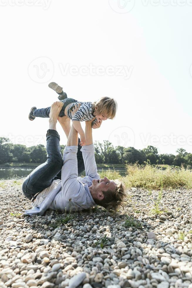 padre e figlio avendo divertimento a il riva del fiume, giocando aereo foto