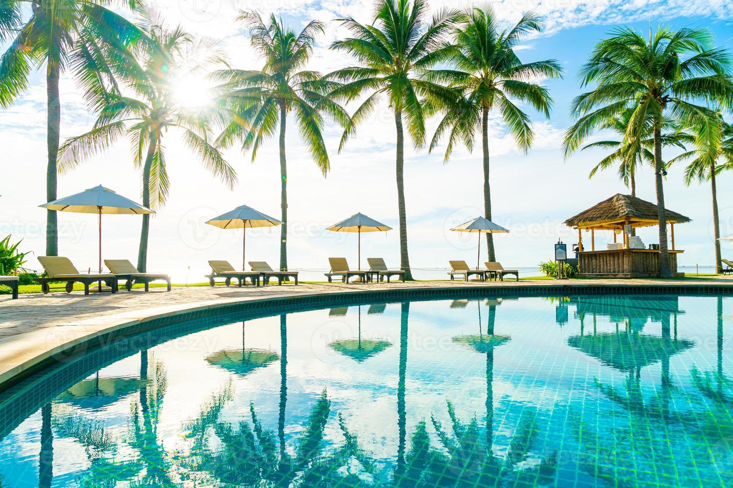 bellissimo ombrellone di lusso e sedia intorno alla piscina all'aperto in hotel e resort con palme da cocco su cielo blu foto