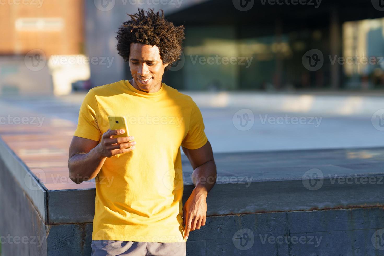 uomo di colore che consulta il suo smartphone mentre si riposa dal suo allenamento. foto
