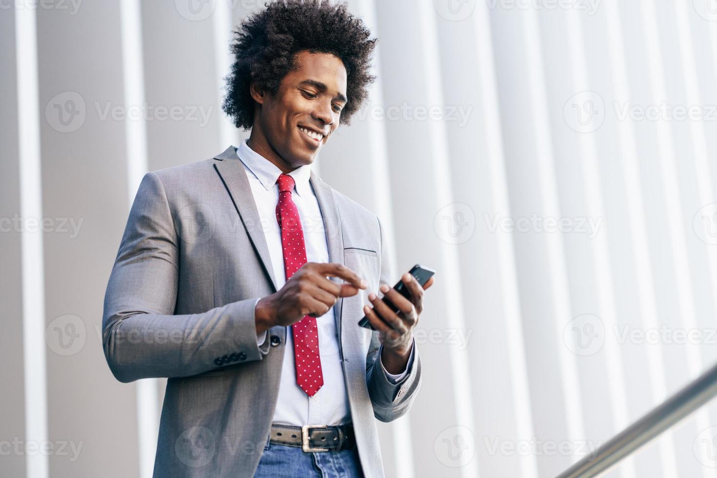 uomo d'affari nero che usa uno smartphone vicino a un edificio per uffici foto