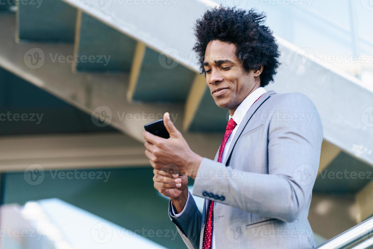 uomo d'affari nero che usa uno smartphone vicino a un edificio per uffici foto