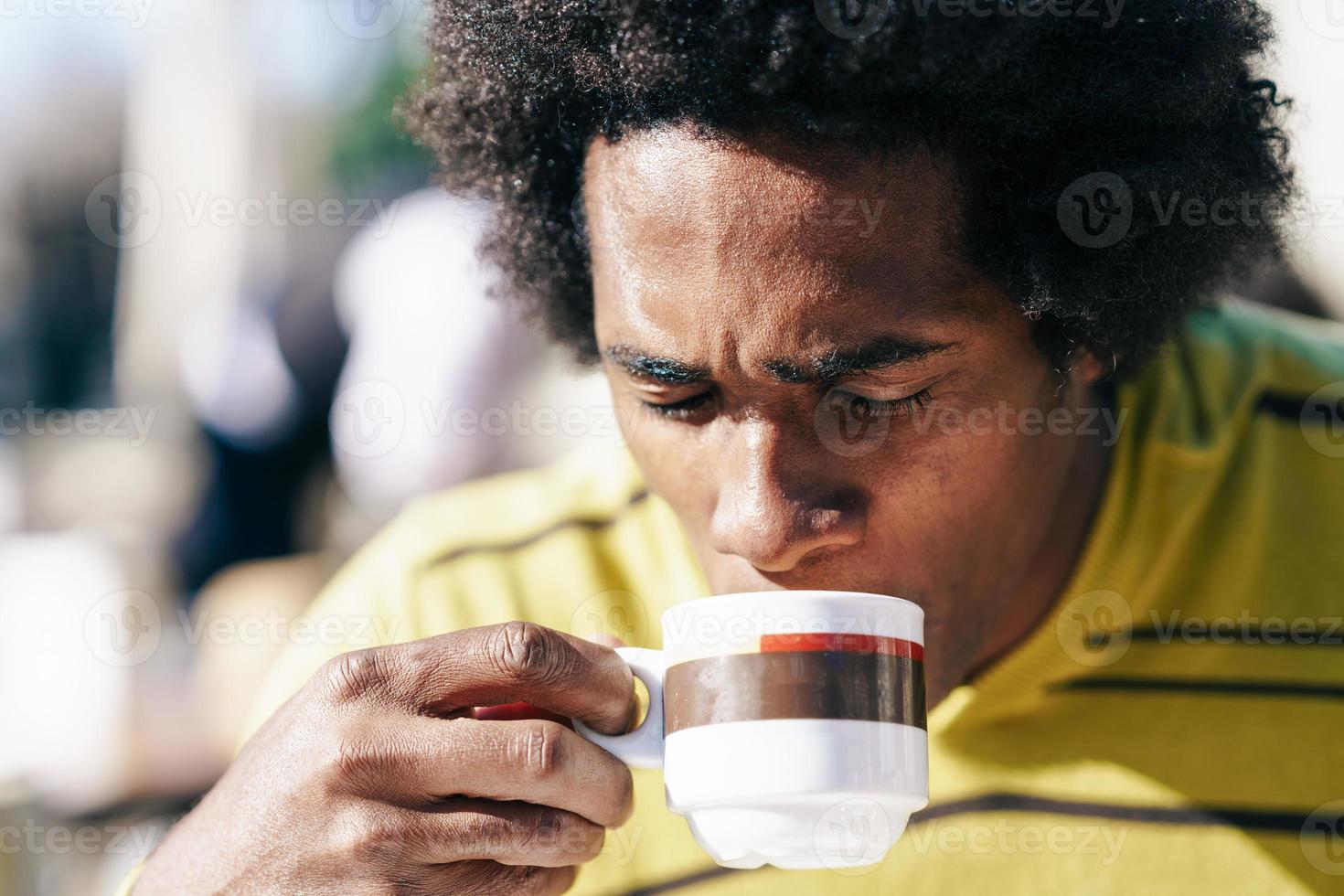 uomo di colore che si gode il caffè al bar mentre è seduto al tavolo all'aperto foto