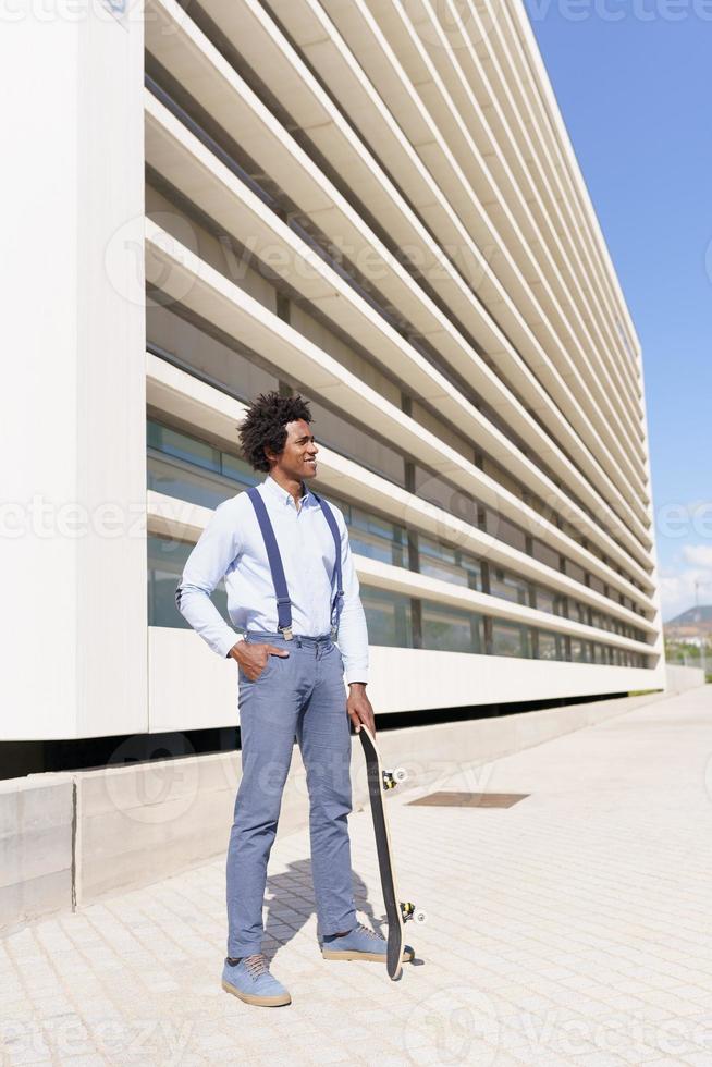 maschio nero in piedi accanto a un edificio per uffici con uno skateboard. foto