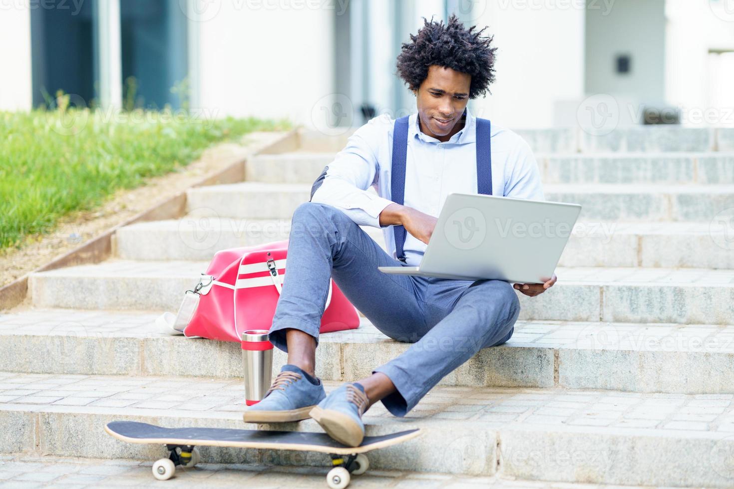 uomo d'affari nero con skateboard usando il suo laptop foto