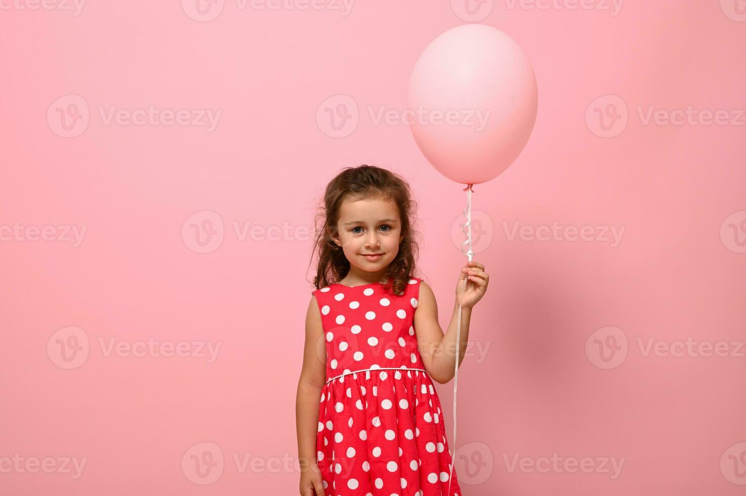 ritratto di un' bellissimo bella bellissima adorabile 4 anni compleanno ragazza, bambino nel vestito con Pois modello, Tenere un' rosa Palloncino, isolato su rosa sfondo con copia spazio per pubblicità. foto