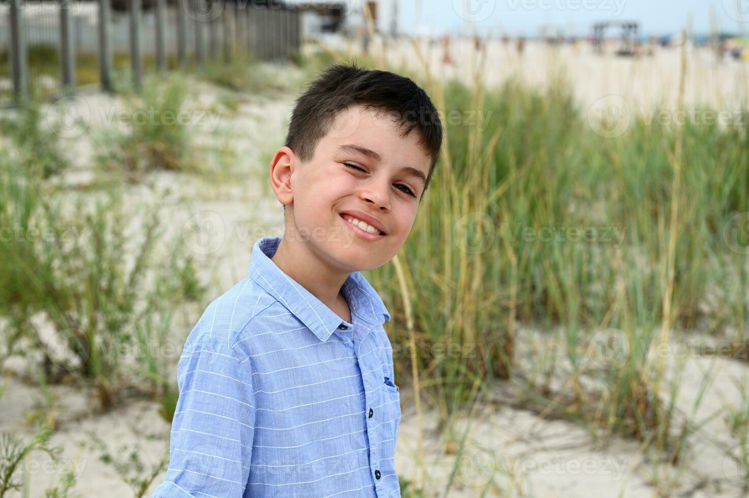 colpo alla testa di adorabile ragazzo carino sorridente in piedi contro il fondale di steppa boschetti e sabbioso suolo. bello bambino carino sorrisi guardare a il telecamera. foto