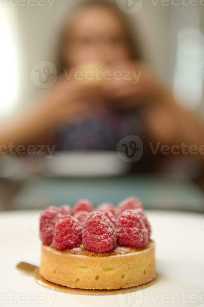 dettagli su un' francese dolce - un' tortino con lamponi su un' bianca piatto, al di sopra di sfocato sfondo di un' poco bambino foto