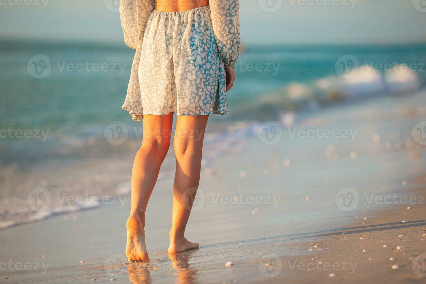 femmina gambe su il spiaggia avvicinamento. donna nel vestito a piedi su il spiaggia foto