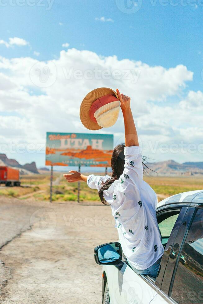 bellissimo donna su sua viaggio di il macchina. benvenuto per Utah strada cartello. grande benvenuto cartello saluta viaggi nel monumento valle, Utah foto