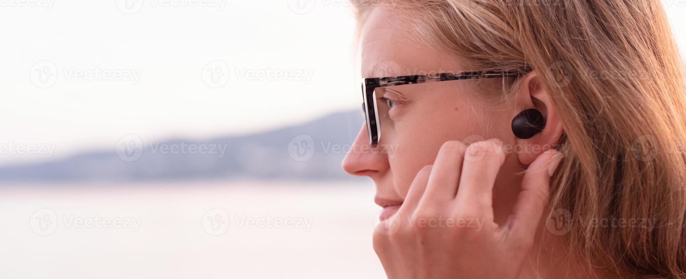 donna che utilizza auricolari wireless, mare sullo sfondo foto
