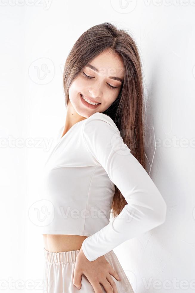 ragazza felice in pigiama bianco in piedi vicino al muro a casa sorridente foto