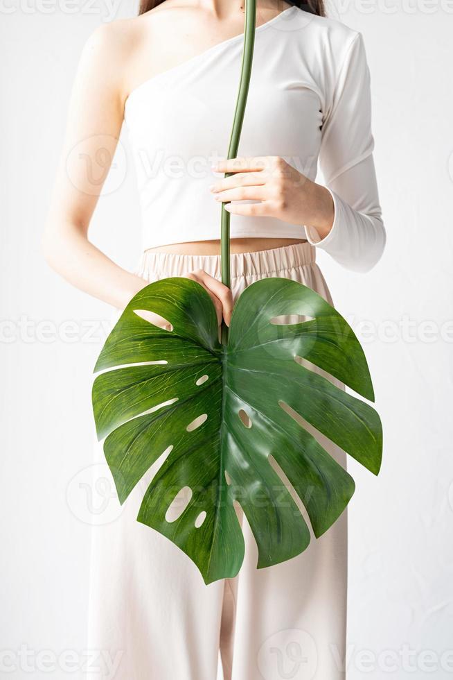 bella donna felice in abiti comodi che tiene una foglia verde di monstera green foto